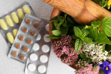 Wooden mortar with fresh herbs, flowers and pills on white table, top view