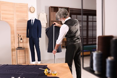 Photo of Professional tailor with measuring tape working in atelier