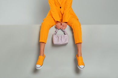 Young woman wearing stylish orange clothes with bag on grey background, closeup
