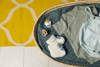 Basket with baby clothes and accessories on floor, top view. Space for text