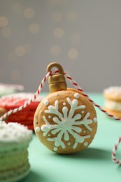 Photo of Beautifully decorated Christmas macarons with rope on turquoise table against blurred festive lights, closeup