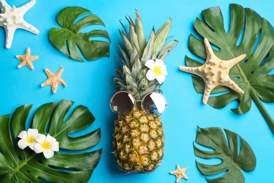 Flat lay composition with pineapple, sunglasses and beach items on light blue background. Creative concept