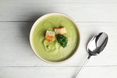Delicious broccoli cream soup with croutons served on white wooden table, flat lay