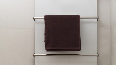 Brown soft towel on modern heated rail in bathroom, space for text