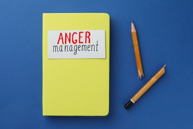 Notebook with words Anger Management and broken pencil on blue background, flat lay