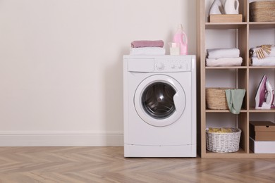 Laundry room interior with modern washing machine and shelving unit near white wall. Space for text