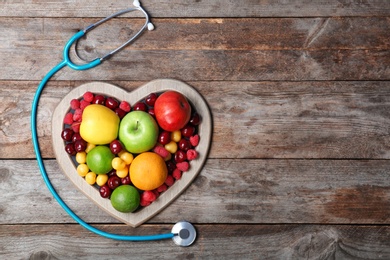 Heart shaped plate with fresh fruits and stethoscope on wooden table, top view. Cardiac diet