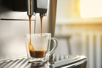 Espresso machine pouring coffee into glass cup against blurred background, closeup. Space for text