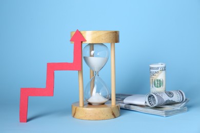 Economic profit. Hourglass, banknotes and arrow on light blue background