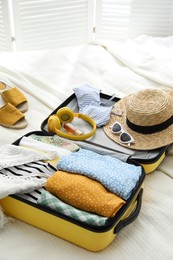 Open suitcase full of clothes, shoes and summer accessories on bed