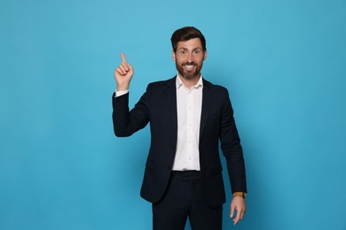 Photo of Smiling bearded man pointing index finger up on light blue background