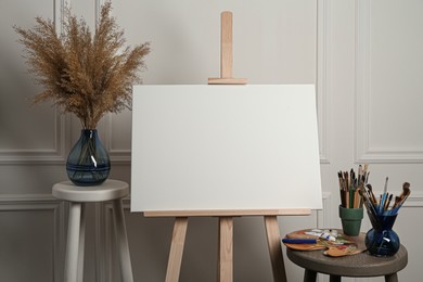 Easel with blank canvas, brushes, paints and palette in studio