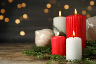 Photo of Burning candles and festive decor on wooden table against blurred Christmas lights, space for text
