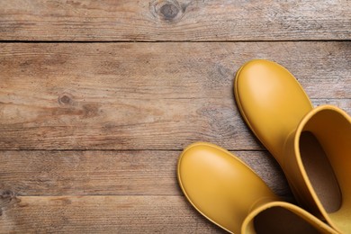 Yellow rubber boots on wooden background, top view. Space for text