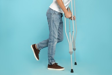 Man with injured leg using crutches on turquoise background, closeup