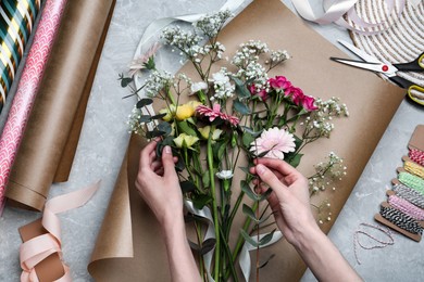 Photo of Woman arranging flowers at grey stone table, top view