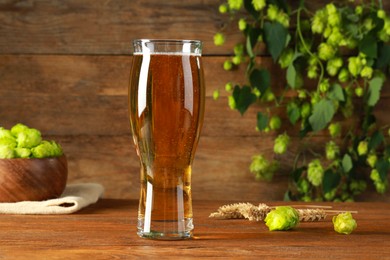 Photo of Glass of beer, fresh green hops and spikes on wooden table
