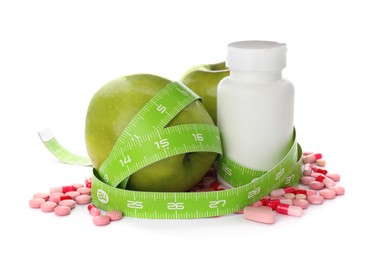 Weight loss pills, apples and measuring tape on white background
