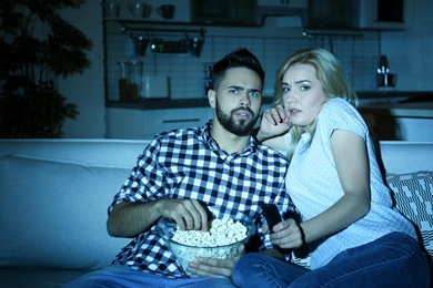 Photo of Young couple with bowl of popcorn watching TV on sofa at night