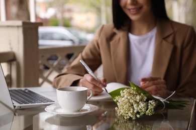 Woman with cup of coffee working at outdoor cafe in morning, closeup