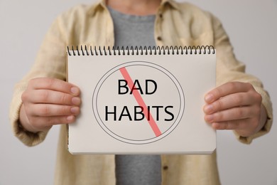 Woman holding notebook with prohibited symbol and phrase Bad Habits against light background, closeup