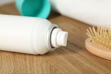 Photo of Bottle of dry shampoo and hairbrush on wooden table, closeup