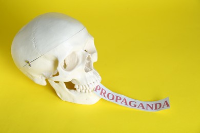 Photo of Information warfare concept. Human skull and paper card with word Propaganda on yellow background