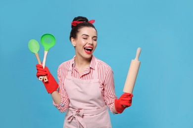 Young housewife with cooking utensils on light blue background