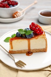 Photo of Slice of delicious cheesecake served with berries and caramel sauce on table, closeup