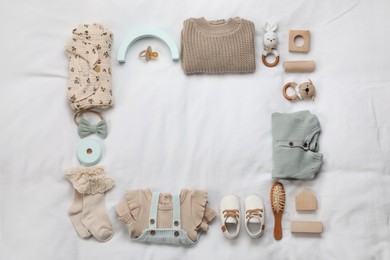 Layout with baby outfit and cute accessories on white bed, top view. space for text