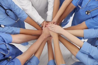 Photo of Doctor and interns stacking hands together indoors, above view