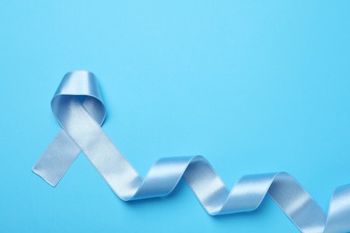 Photo of Light blue awareness ribbon on color background, top view. Space for text