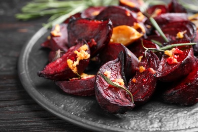 Roasted beetroot slices, garlic and rosemary on black wooden table, closeup