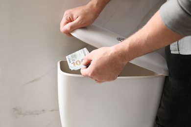 Man hiding money in toilet tank indoors, closeup. Financial savings