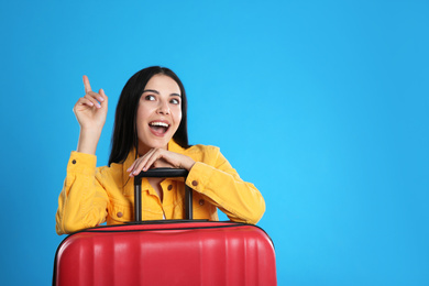 Beautiful excited woman with suitcase for summer trip on blue background, space for text. Vacation travel