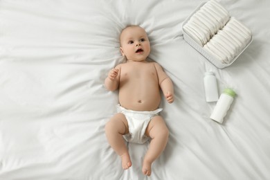 Photo of Cute baby, diapers and cosmetic products on white bed, top view