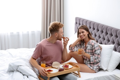 Happy young couple having romantic breakfast on bed at home
