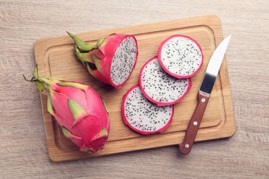 Board with delicious white pitahaya fruits and knife on wooden table, top view