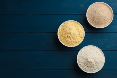 Different types of flours in bowls on blue wooden table, flat lay. Space for text