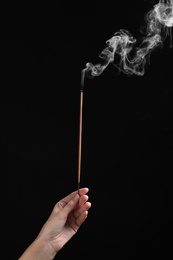 Photo of Woman holding smoldering incense stick on black background, closeup