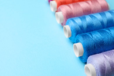 Set of different colorful sewing threads on light blue background, closeup. Space for text