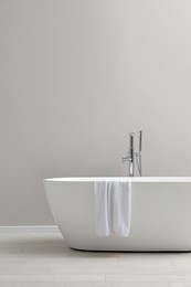 Modern ceramic bathtub with towel near light wall indoors