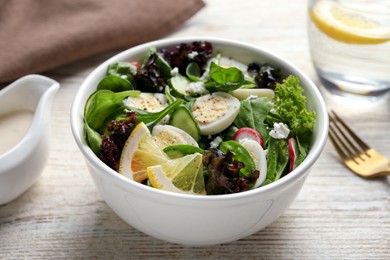 Delicious salad with boiled eggs, vegetables and lemon in bowl on white wooden table, closeup