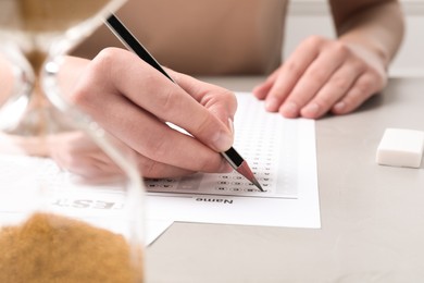 Photo of Student filling answer sheet at light grey table, closeup. Passing exam