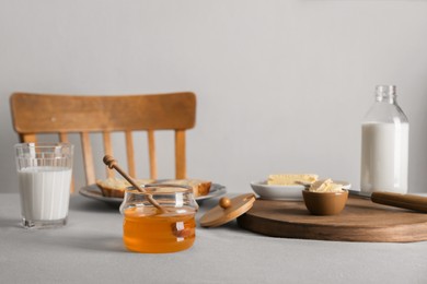 Photo of Jar with honey, milk, butter and bread served for breakfast on grey table