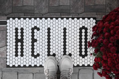 Stylish door mat with word Hello, shoes and beautiful flowers on stairs, flat lay