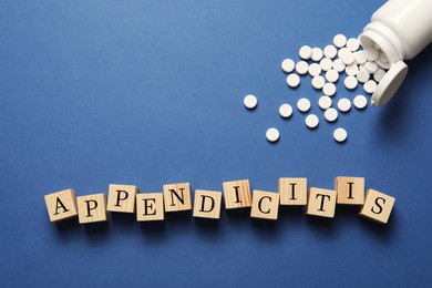 Word Appendicitis made of wooden cubes and jar with pills on blue background, flat lay. Space for text
