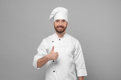 Photo of Smiling mature male chef showing thumbs up on grey background