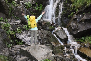 Happy tourist with backpack near mountain waterfall, back view