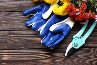 Photo of Gardening gloves, pruner and flowers on wooden table, flat lay. Space for text